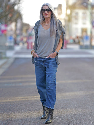 OFF#DLY Strick Top Luna taupe, getragen von einer Frau in Jeans, schmal geschnitten mit feinen Trägern, geeignet bis Größe 42, aus 100% Baumwolle, auf einer Straße stehend.