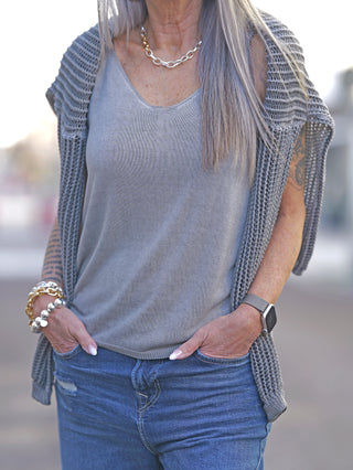 Frau trägt das OFF#DLY Strick Top Luna taupe mit schmalen Trägern, kombiniert mit Jeans. Im Vordergrund sind Details wie ein Armband und eine Kette sichtbar.