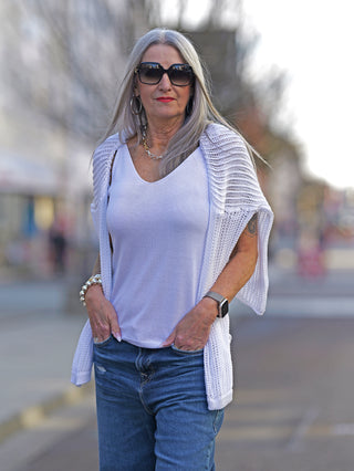 Frau trägt OFF#DLY Strick Top Luna white, ein feinstrick Top mit schmalen Trägern. Kombiniert mit blauer Jeans, Sonnenbrille und Armband, vermittelt es einen lässigen, modischen Look.