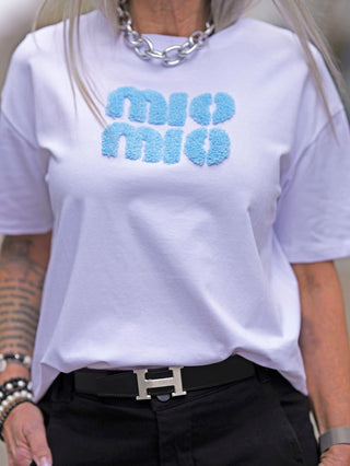Frau trägt das OFF#DLY Tee Iris white/blue mit Teddy-Print. Das Kurzarm T-Shirt hat eine gerade Passform und wird von einem schwarzen Gürtel mit silberner Schnalle ergänzt.