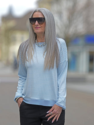 Frau mit grauem Haar trägt Sonnenbrille und das OFF#DLY Ringel Tee Klara blue/white, ein gestreiftes Langarmshirt mit Rundhalsausschnitt und Tüllbündchen.