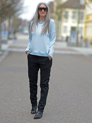 Frau mit langen grauen Haaren trägt das OFF#DLY Ringel Tee Klara blue/white, ein gestreiftes Langarmshirt mit Rundhals und Tüllbündchen, passend für lässige Straßenmode.