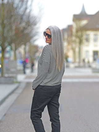Frau mit grauem Haar trägt das OFF#DLY Ringel Tee Klara black/white, ein gestreiftes Longsleeve mit Tüllbündchen, auf der Straße. Perfekt für lässige Mode.