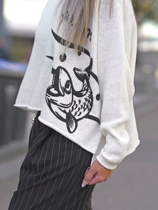 Rundholz Pulli 3720701: Frau in weißem Pullover mit schrägem Schnitt und seitlichem Fisch-Black-Print, klassischer Rundhalsausschnitt, Boxy Passform, avantgardistisches Design.