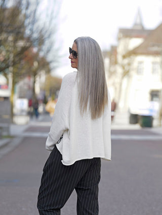 Frau mit langen grauen Haaren trägt den Rundholz Pulli 3720701, erkennbar durch schrägen Schnitt und seitlichen Fisch-Print, kombiniert mit weißem Sweater und gestreiften Hosen.