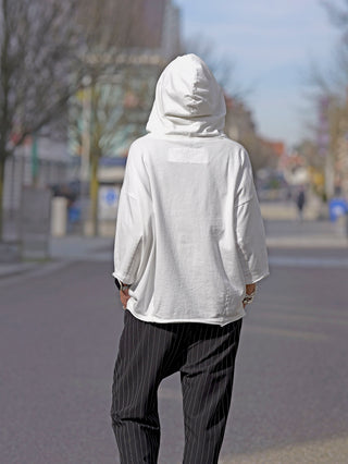 Eine Person trägt das Rundholz Tee 3290502 in Offwhite mit auffälligem Print, während sie auf der Straße geht, kombiniert mit eleganten pinstriped Pants und einem weißen Hoodie.