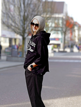 Frau in schwarzem Rundholz Tee 3290502, oversized Passform, trägt Sonnenbrille und schwarze Hose, steht lässig auf der Straße. Perfekt für avantgardistische Mode-Enthusiasten.