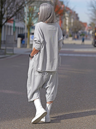 Rundholz Tee 3290524 grey: Person trägt graues Longsleeve mit offenen Saumkanten und Rundhalsausschnitt, kombiniert mit weißen Stiefeln auf der Straße.