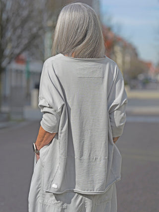 Rundholz Tee 3290524 grey: Frau mit grauem Longsleeve, lockerem Schnitt und offenen Saumkanten, trägt eine Armbanduhr. Das Shirt hat seitliche Einschubtaschen und einen Rundhalsausschnitt.