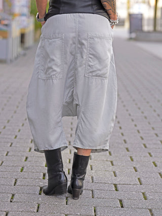 Person trägt die Rundholz Hose 3200104 in Grau mit weitem Bein, verkürztem Schnitt und seitlichen Taschen, kombiniert mit schwarzen Stiefeln.