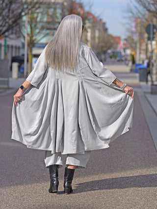 Frau trägt das Rundholz Kleid 3200906 in Grau als Kleid, kombiniert mit langen Boots. Sichtbar sind die lange Silhouette und die durchgehende Knopfleiste des wandelbaren Designs.