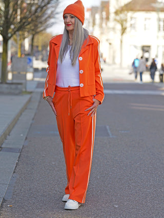 Frau trägt OFF#DLY Pant Stripes orange, weite Hose mit sportlichen Streifen und elastischem Bund, kombiniert mit passendem orangefarbenem Blazer für dynamischen, trendbewussten Look.