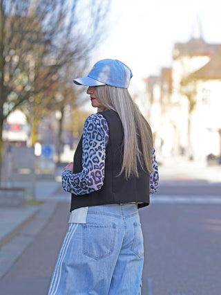 Frau trägt die OFF#DLY Weste Sonja black, eine elegant taillierte schwarze Anzugweste mit Knopfverschluss, kombiniert mit blauer Jeans und blauem Hut, ideal für modernen Street-Style.