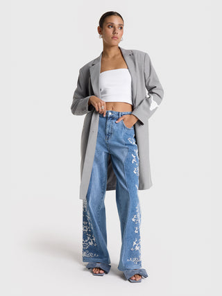 ALIX Clean Long Blazer grey, getragen von einer Frau, mit Fronttaschen und Knopfverschluss. Der Blazer hat eine übergroße Passform, reicht über die Knie und wird mit blauer Jeans kombiniert.