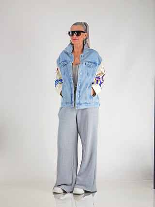 ALIX Mixed Sleeves Denim Jacket denimblue: Frau trägt übergroße, stilvolle Denimjacke mit gemischten Ärmeln und auffälligen Applikationen, ergänzt durch lässige graue Hosen und weiße Turnschuhe.