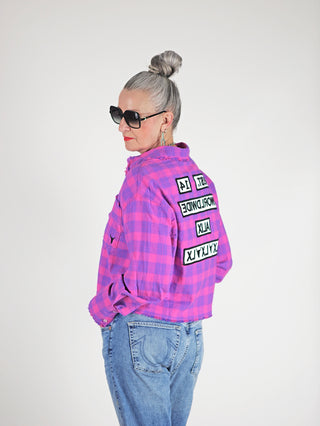 Frau trägt ALIX Cropped Ceck Bluse pink mit übergroßer Passform und ausgefranstem Saum, kombiniert mit Jeans und Sonnenbrille für einen lässigen, modernen Look.