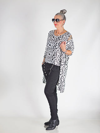 Frau trägt das OFF#DLY Leo Set Raelle weiß, bestehend aus lockerem Top und langem Cardigan mit Schwarz-Weiß-Print, kombiniert mit schwarzer Hose für eleganten Look.