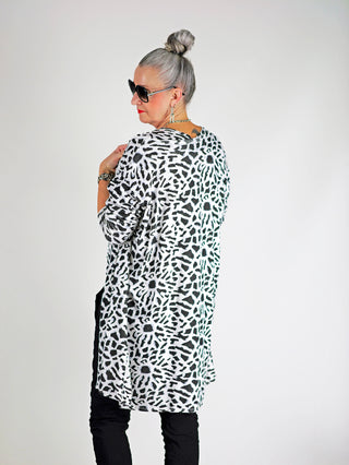 Frau trägt das OFF#DLY Leo Set Raelle weiß, bestehend aus einem locker geschnittenen Top und langem Cardigan mit schwarz-weißem Print, ideal für einen stilvollen, modernen Look.