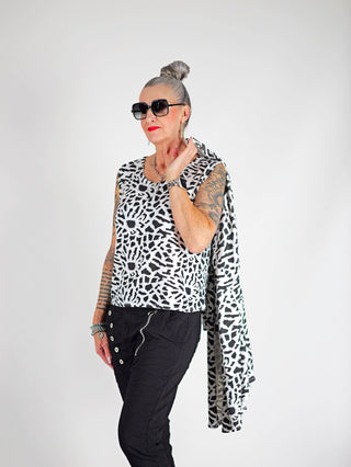 Frau mit Tattoos trägt das OFF#DLY Leo Set Raelle weiß, bestehend aus lockerem Top und langem Cardigan mit Schwarz-Weiß-Print, kombiniert mit Sonnenbrille und roten Lippen.