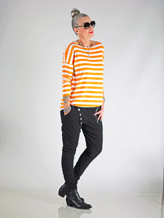 OFF#DLY Ringel Grosso white/orange: Frau trägt gestreiftes Langarmshirt mit Rundhalsausschnitt und langen Ärmeln, kombiniert mit schwarzer Hose und Sonnenbrille. Lockerer Schnitt für lässigen Stil.