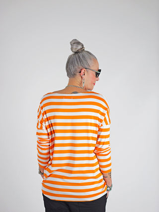Frau trägt OFF#DLY Ringel Grosso white/orange Langarmshirt, locker geschnitten, mit Rundhalsausschnitt und Streifenmuster, kombiniert mit Sonnenbrille. Ideal für einen lässigen, stilvollen Look.