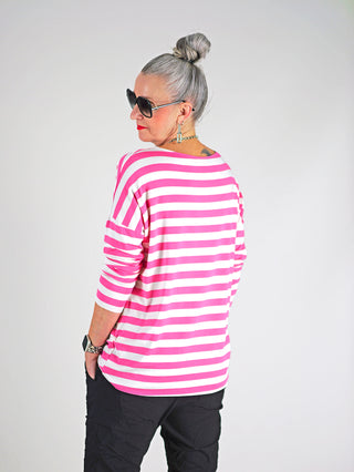 Frau trägt OFF#DLY Ringel Grosso Langarmshirt in weiß/pink mit Streifen, lockerer Passform und Rundhalsausschnitt. Kombiniert mit Sonnenbrille, unterstreicht das lässige, stilvolle Design.