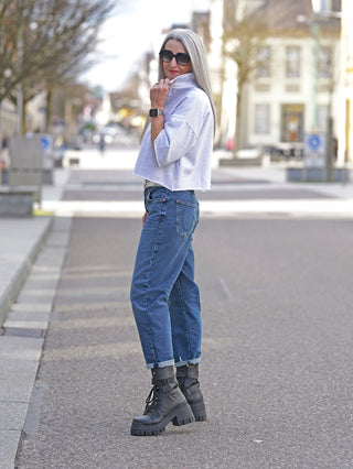 Frau in blauer Jeans trägt #VDR Polo Sweater grey melange, ein cropped Sweatshirt mit modernen oversized Ärmeln und Polokragen, ideal kombiniert mit High-Waist-Jeans für einen trendigen Look.