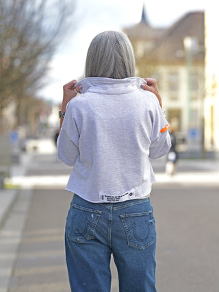 Frau trägt #VDR Polo Sweater grey melange mit modernem Cropped-Schnitt und Oversized-Ärmeln, kombiniert mit blauer Jeans. Der dezente Polokragen verleiht dem Outfit einen stilvollen Touch.