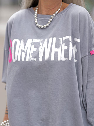 #VDR Sweat grey: Person trägt grauen Oversize-Sweater mit weiß-pinkem Statement-Print „SOMEWHERE“ und pinkem #VDR-Label am Ärmel. Lässiger Look mit einer Kette kombiniert.