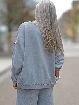 Frau mit langem Haar trägt #VDR Sweat grey Oversize-Sweater mit weißem und pinkem Statement-Print SOMEWHERE, pinkes #VDR-Label am Ärmel sichtbar.