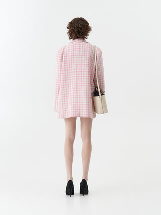 Lumina Blazer rose: Frau trägt einen Bouclé-Blazer mit zartem Karo-Muster in Rosé und Creme. Der elegante, oversized Schnitt betont eine moderne Silhouette, kombiniert mit Fischernetzstrumpfhosen.