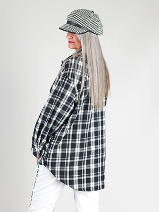 Frau trägt Off#DLY Shirt Canada black/white, eine oversized Hemdjacke mit schwarzem und weißem Karomuster und Print-Details, langen Ärmeln und Knopfleiste, aus 100 % Baumwolle.