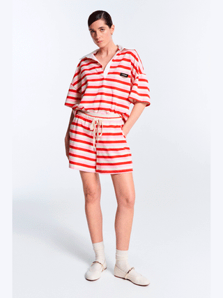 Lumina Polo Bluse pink/red: Frau trägt gestreiftes, oversized Poloshirt mit roten und weißen Streifen, kombiniert mit Shorts. Lässiger, modischer Look inspiriert von aktuellen Streetstyle-Trends.