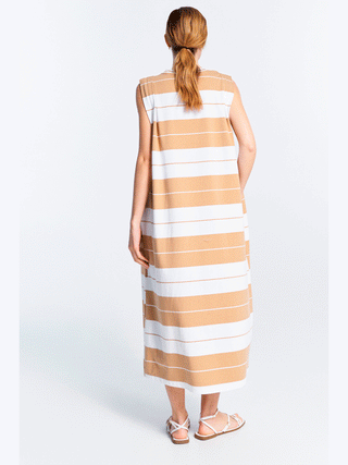 Frau in einem ärmellosen Lumina Dress Stripes caramel mit Streifenmuster, das locker fällt. Trägt Sandalen, Haare im Pferdeschwanz. Perfekt für sonnige Tage, aus Baumwollmix.