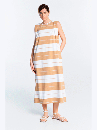 Frau trägt Lumina Dress Stripes caramel, ärmelloses Maxikleid mit Streifenmuster. Das Kleid hat einen lockeren Schnitt und Rundhalsausschnitt, ideal für warme Tage und vielseitige Looks.