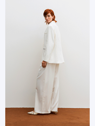 Lumina Blazer white: Frau im weißen Blazer mit geradem, leicht oversized Schnitt und feinen Kontrastnähten. Der Blazer präsentiert eine stilvolle Eleganz, ideal für Business und Alltag.