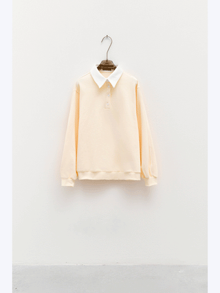 Lumina Sweat offwhite/crema: Langarm-Pullover-Polo mit weißem Kragen und Drei-Knopf-Leiste, präsentiert auf dunklem Haken. Baumwollmaterial für Komfort und vielseitigen, eleganten Look.