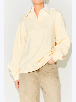 Das Bild zeigt den Lumina Sweat offwhite/crema, einen locker sitzenden, cremefarbenen Baumwollpullover mit weißem Polokragen und Dreiknopfleiste, kombiniert mit hellbeigen, hochgeschnittenen Jeans.
