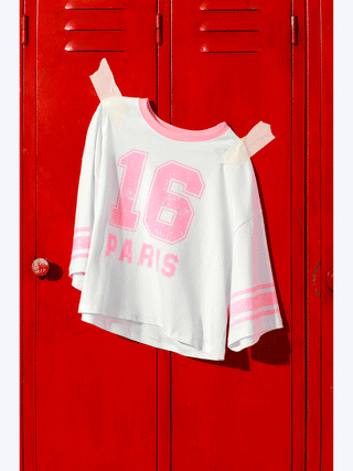 Lumina Sporty Shirt pink, ein oversized Baumwoll-T-Shirt mit pinkem 16 PARIS Frontprint und kontrastierenden Streifen, präsentiert sich vor einem roten Hintergrund, ideal für einen lässigen Athleisure-Look.