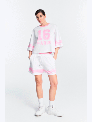 Lumina Sporty Shirt pink, getragen von einer Person. Weißes, oversized Baumwoll-T-Shirt mit pinkem 16 PARIS Frontprint und kontrastierenden Streifen an Ärmeln, ideal für sportlichen Streetstyle.