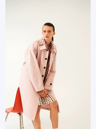 Lumina Mantel Rose: Frau in rosa Trenchcoat mit schwarzem Knöpfen und Taillengürtel, zeigt klassischen Schnitt und moderne Details, ideal für elegante oder legere Looks.
