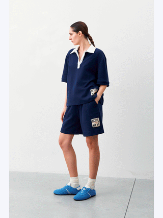 Lumina Activ Short blue: Frau in blauer Shorts mit „Active Wear“-Patch, kombiniert mit einem blauen Shirt, trägt weiße Socken und blaue Schuhe für einen sportlichen Look.