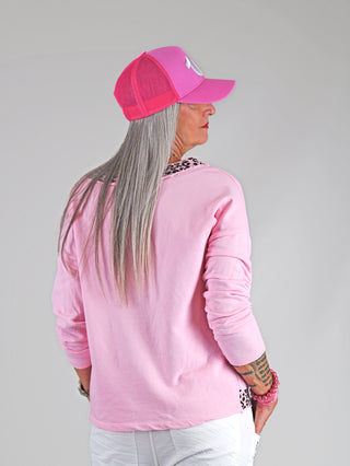 Frau trägt das OFF#DLY Lightsweat Liora rose/leo mit langen Ärmeln, rosa Leo-Details an Ausschnitt und Saum. Kombiniert mit pinkem Hut, ideal für lässigen Chic und Komfort.