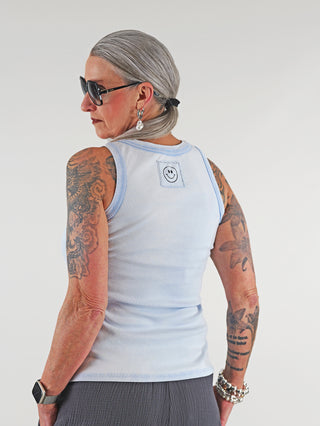 OFF#DLY Top Neve lightblue getragen von tätowierter Frau, mit Smiley-Patch auf der Rückseite. Perfekt für Sommer, mit sportlichem Rundhalsausschnitt und lässigem Stil. Ideal für Größe bis 40.