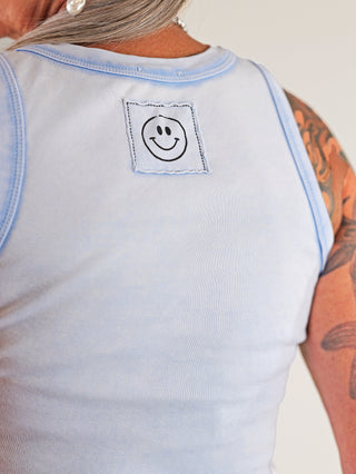Person trägt das OFF#DLY Top Neve lightblue, ein ärmelloses Baumwoll-Top mit einem Smiley-Patch, ideal für lässige Sommerlooks. Perfekte Passform bis Größe 40.