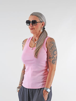 Frau mit Tattoos trägt das OFF#DLY Top Neve rose, ein ärmelloses Baumwoll-Top mit Smiley-Patch, ideal für Sommerkleidung. Kombiniert mit Sonnenbrille und modischem Design.