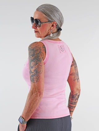 OFF#DLY Top Neve rose: Frau mit grauen Haaren trägt ärmelloses Baumwoll-Top mit Smiley-Patch, zeigt Tattoos am Arm, kombiniert mit Sonnenbrille, das Top ist lässig und modisch.