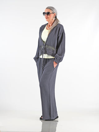 Frau trägt OFF#DLY Musselin Pant Frida anthrazit, eine weite, graue Musselin-Hose mit elastischem Bund und Kordelzug. Die Hose hat eine luftige Passform und Seitentaschen.