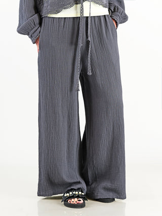 OFF#DLY Musselin Pant Frida anthrazit: Weite, luftige Musselin-Hose mit elastischem Bund und Kordelzug, getragen von einer Person. Sichtbare Details sind die fließende Silhouette und praktische Seitentaschen.