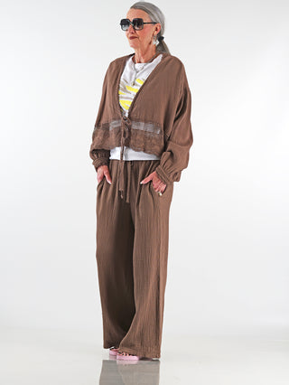 OFF#DLY Musselin Jacke Ritta mokka getragen von einer älteren Frau, zeigt weite Ärmel, zarte Spitzenborte und Bindegürtel, vermittelt feminine Leichtigkeit und luftige Silhouette.